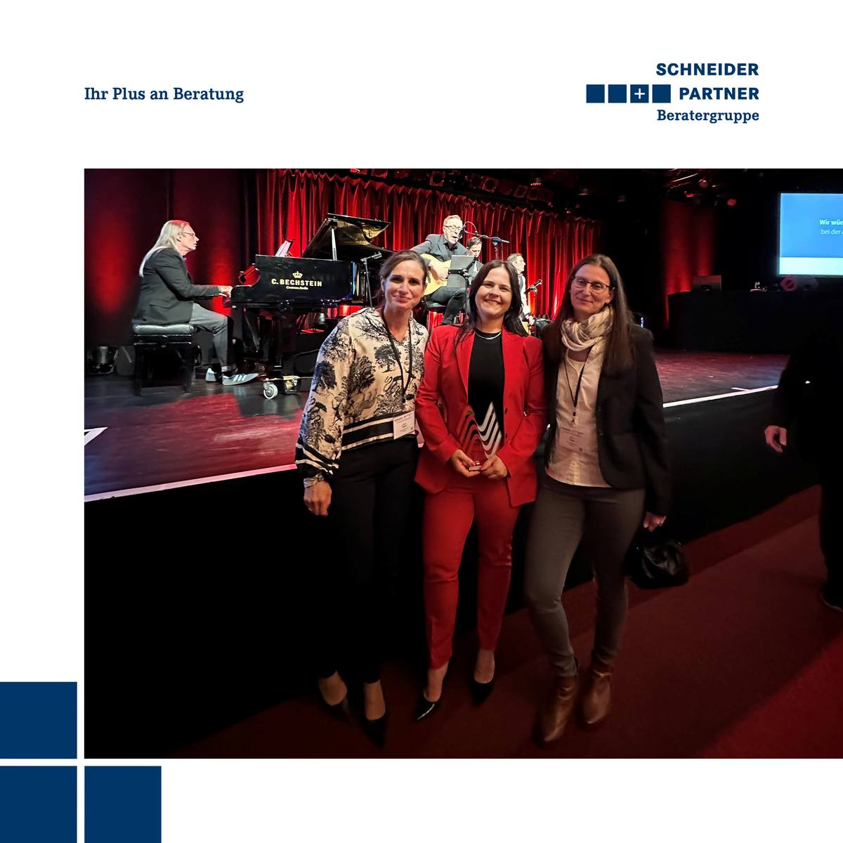 3 Frauen lächeln nach einer Preisverleihung in die Kamera, eine davon hält einen Pokal in der Hand.