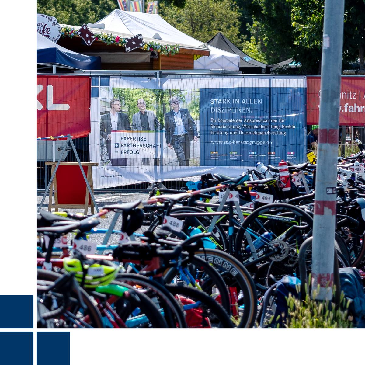 Blick in die Triathlonwechselzone mit Fahrrädern im Vorder- und Zaunwerbung im Hintergrund