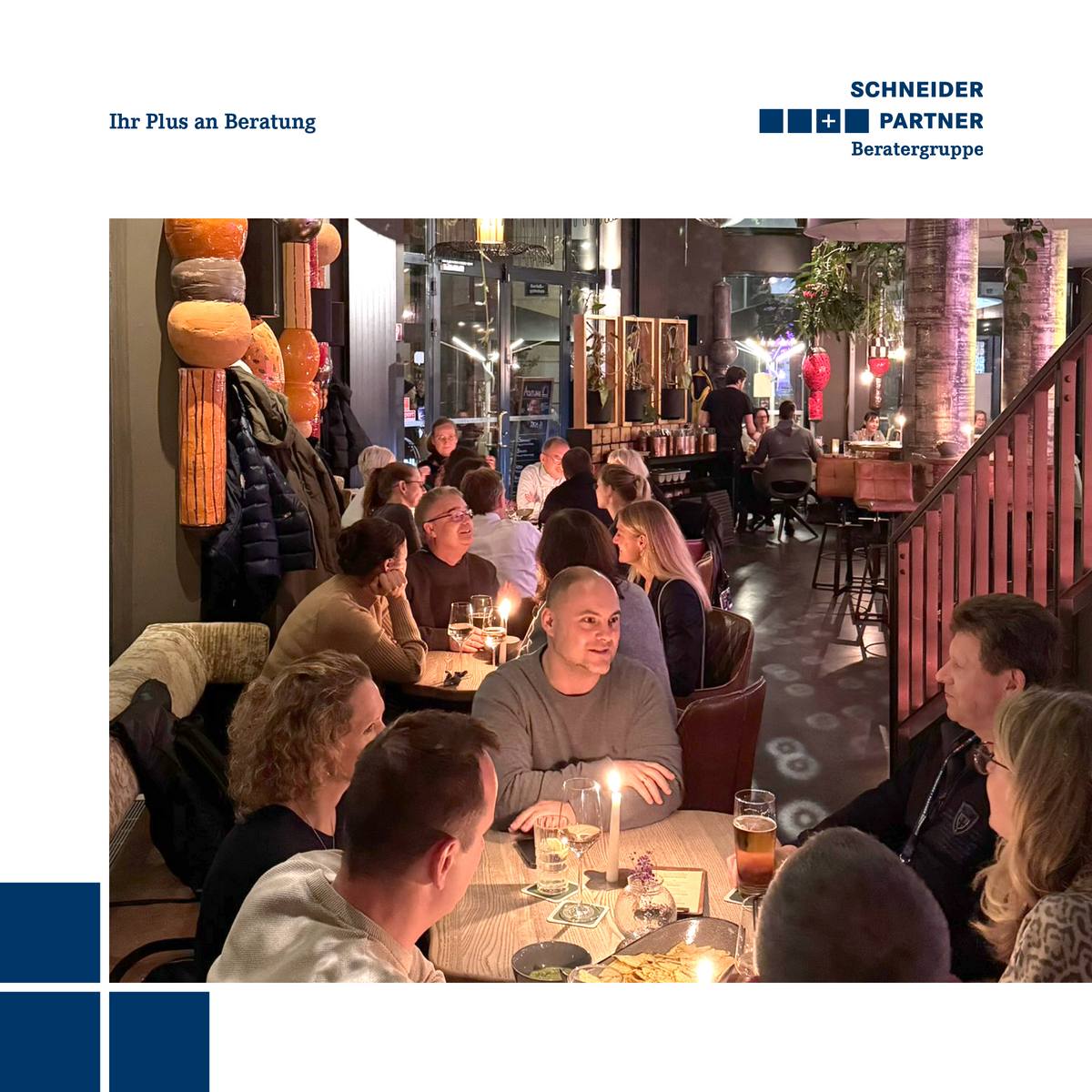 Gemischte Personengruppe sitzt bei abendlicher Beleuchtung an mehreren Tischen in einem Restaurant zusammen.