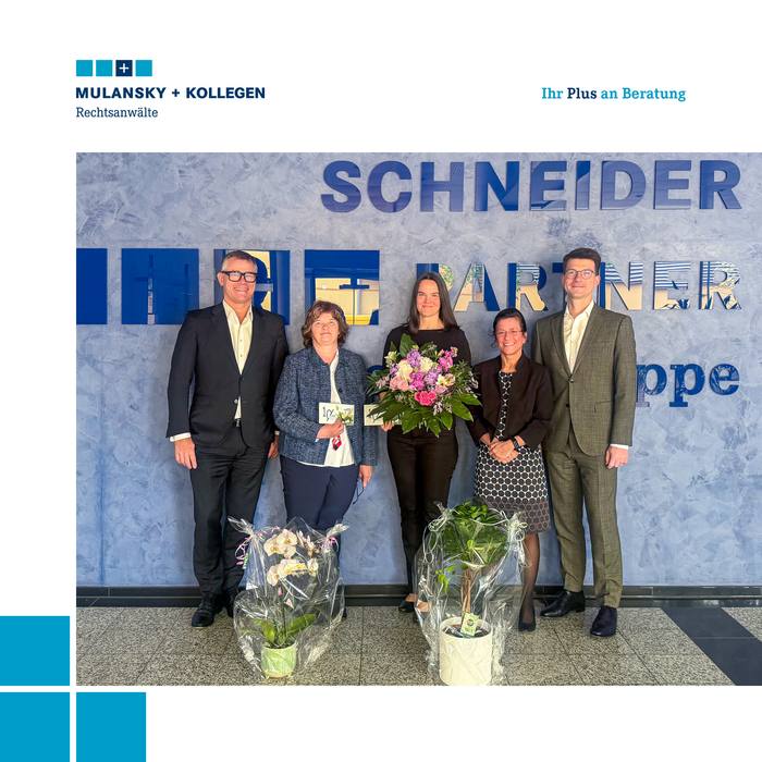 Drei Frauen stehen zwischen zwei Herren, eine hält einen Blumenstrauß, zu Füßen der anderen weitere Blumenpräsente.